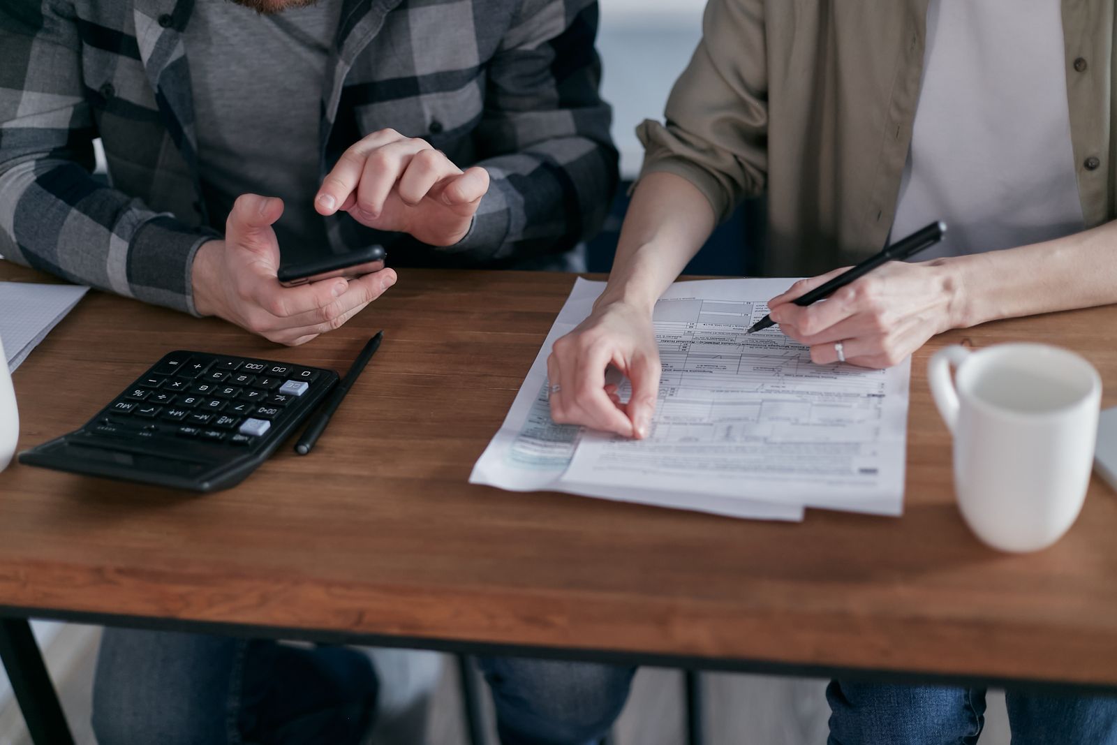 Mãos preenchendo um formulário sobre a mesa, com calculadora e caneta ao lado